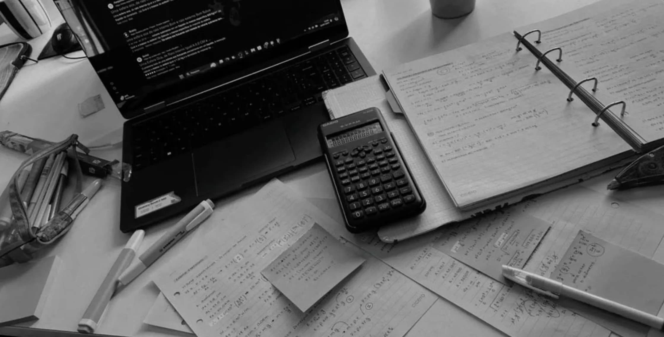 Mesa de estudos com notebook, calculadora e cadernos com anotações